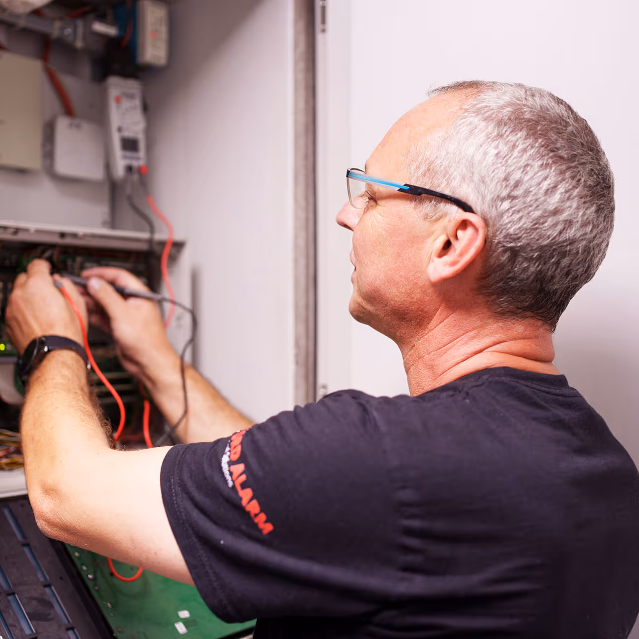 Fachmann für Sicherheitstechnik und Alarmanlagen verkabelt eine Alarmanlage an einem Schaltschrank.